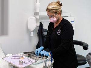 Dental assistant wearing PPE and preparing instruments for emergency dental care