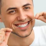 Smiling man holding dental floss to highlight cleaning convenience with Invisalign